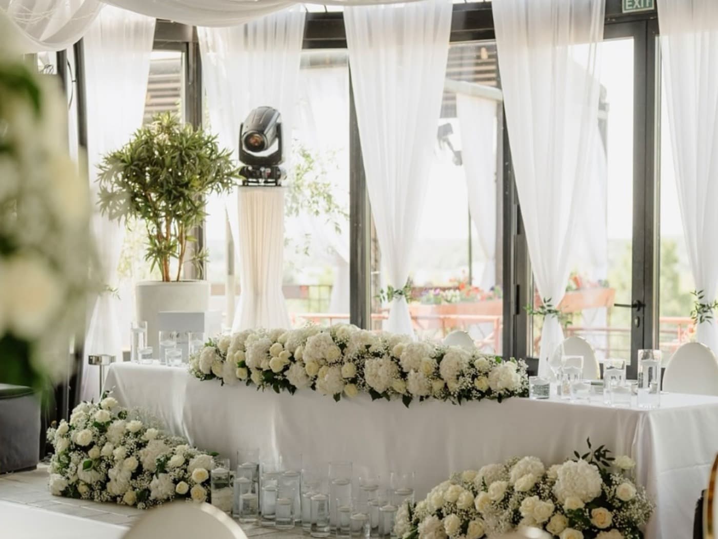 The head table in the conservatory, dressed in white flowers and sheer curtains