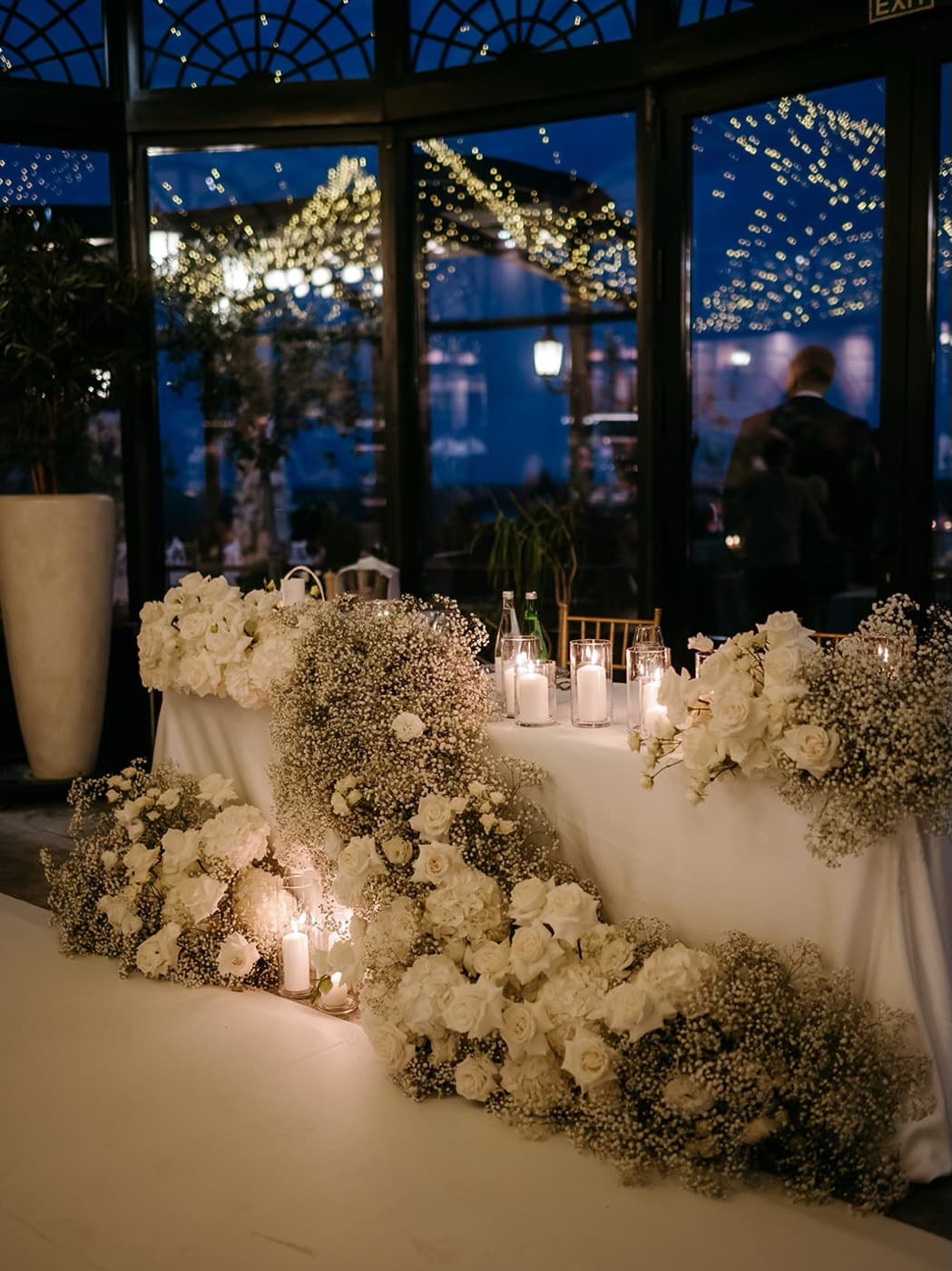 The head table at night, surrounded by white roses and candles